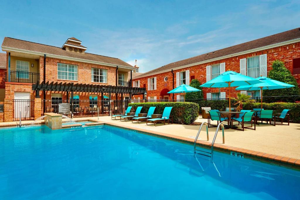a swimming pool with chairs and umbrellas in front of a building at Residence Inn Houston by The Galleria in Houston