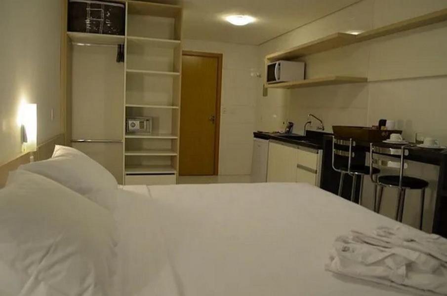 a bedroom with a white bed and a kitchen at Executive 106 Sem Garagem in Caxias do Sul