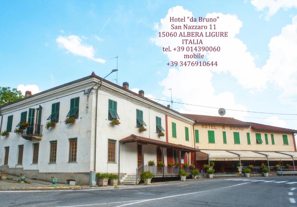 a white building with green shutters on a street at Hotel Da Bruno in Rocchetta Ligure