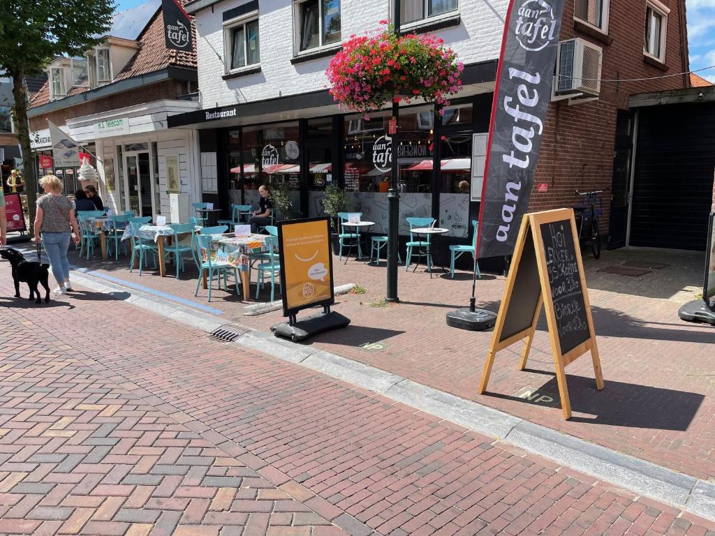 een vrouw die een hond uitlaat op straat met tafels en stoelen bij Restaurant Hostel Aan Tafel in Lunteren