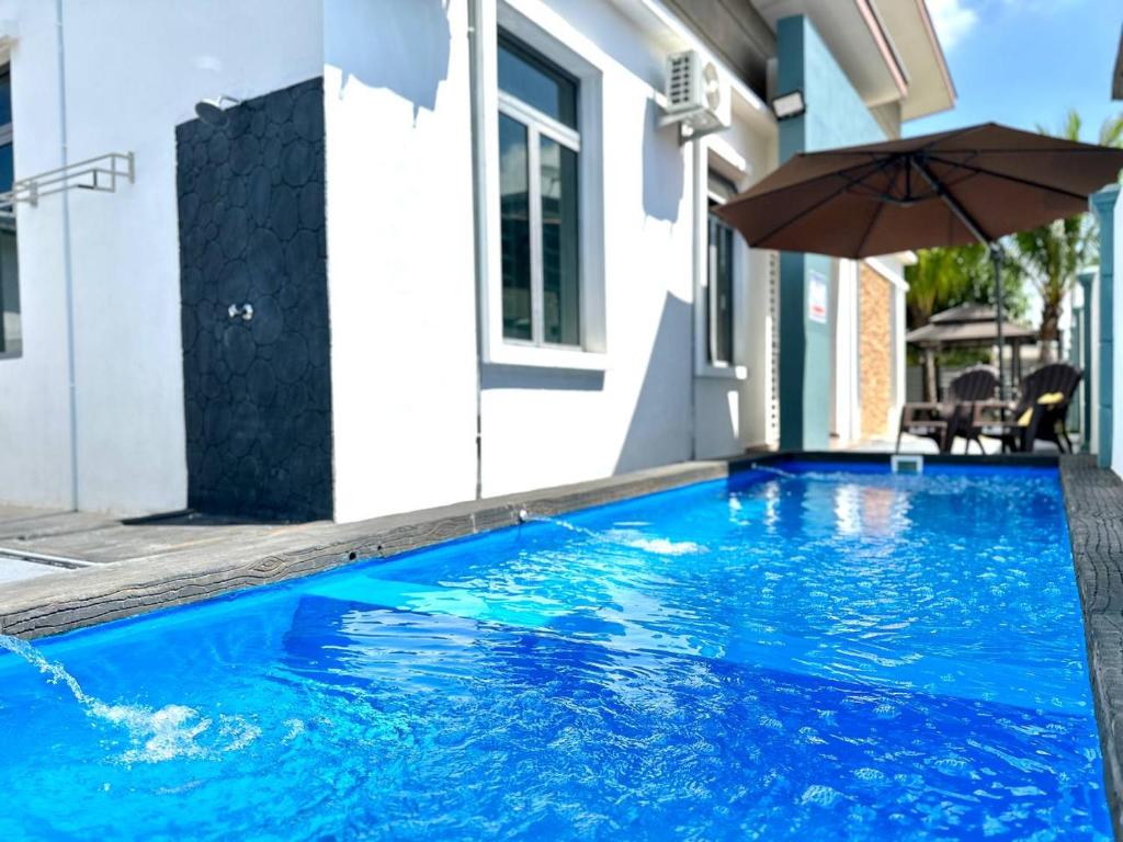 a swimming pool with an umbrella next to a house at Bandar Melaka Family Bungalow Private Pool BBQ WiFi Netflix in Malacca