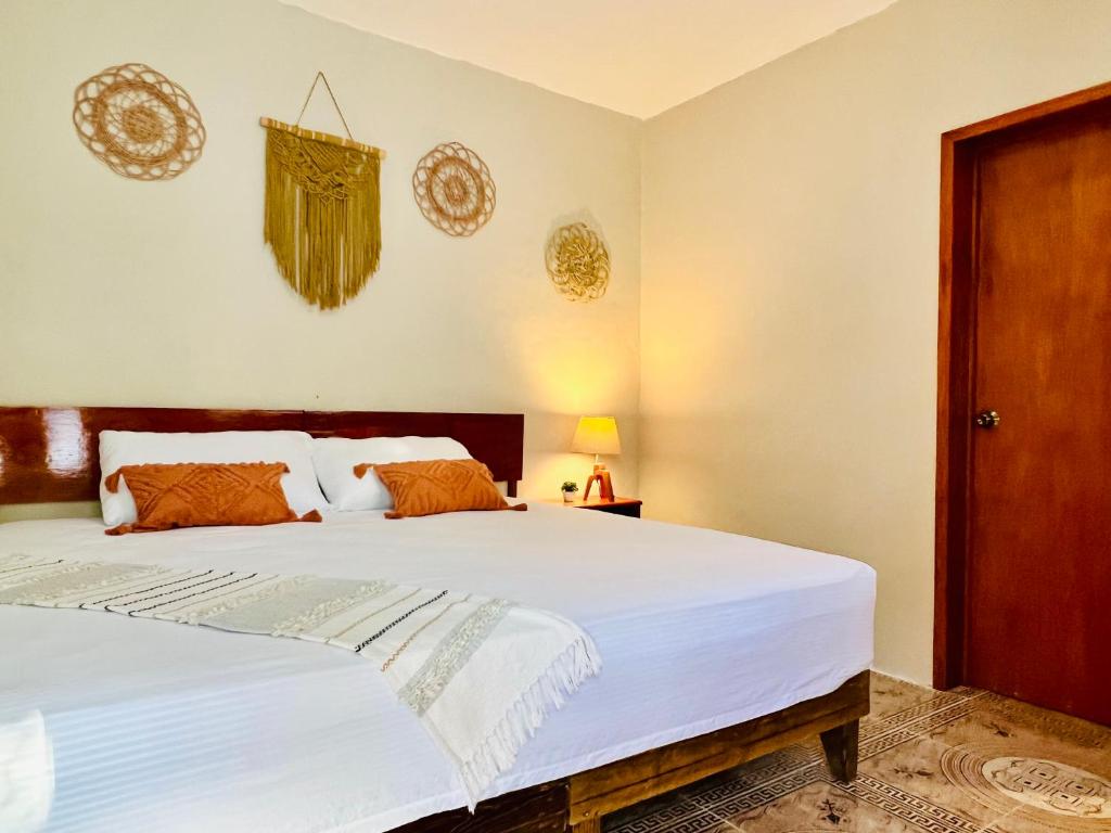 - une chambre dotée d'un grand lit avec des draps blancs et des oreillers orange dans l'établissement CASA VICTORIA, à Chichén Itzá