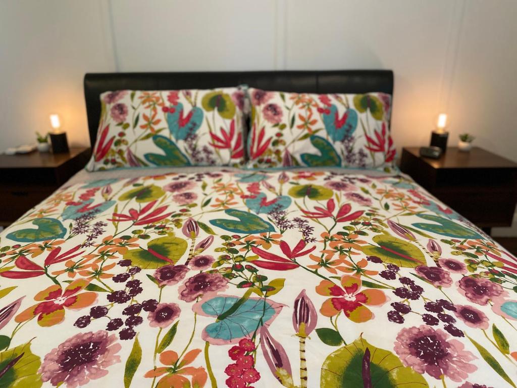 a bed with a flowered comforter with two tables at Wood Cottage in Balingup