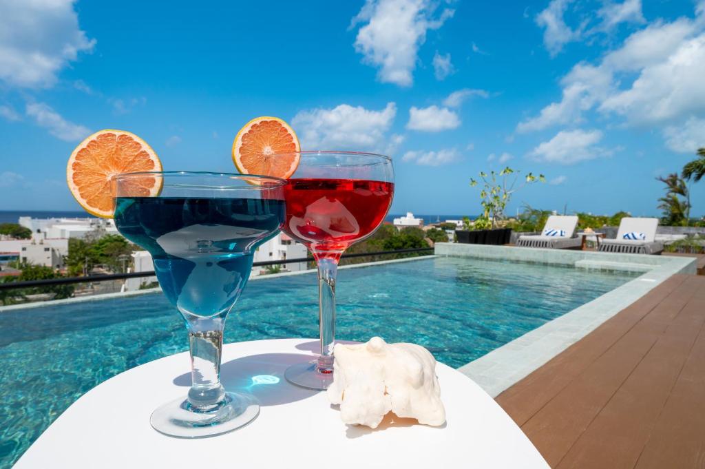 two glasses of wine on a table next to a swimming pool at Kippal - Modern Oasis - ApartHotel in Cozumel