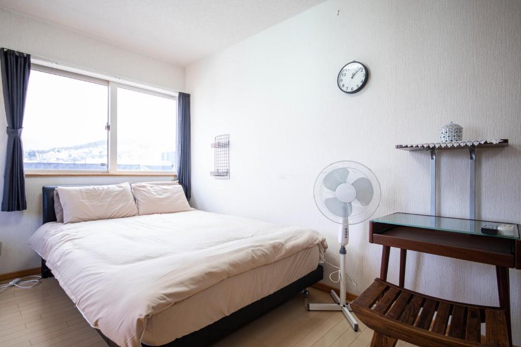 um quarto com uma cama, uma secretária e um relógio em Sumiyoshi House Room B em Otaru