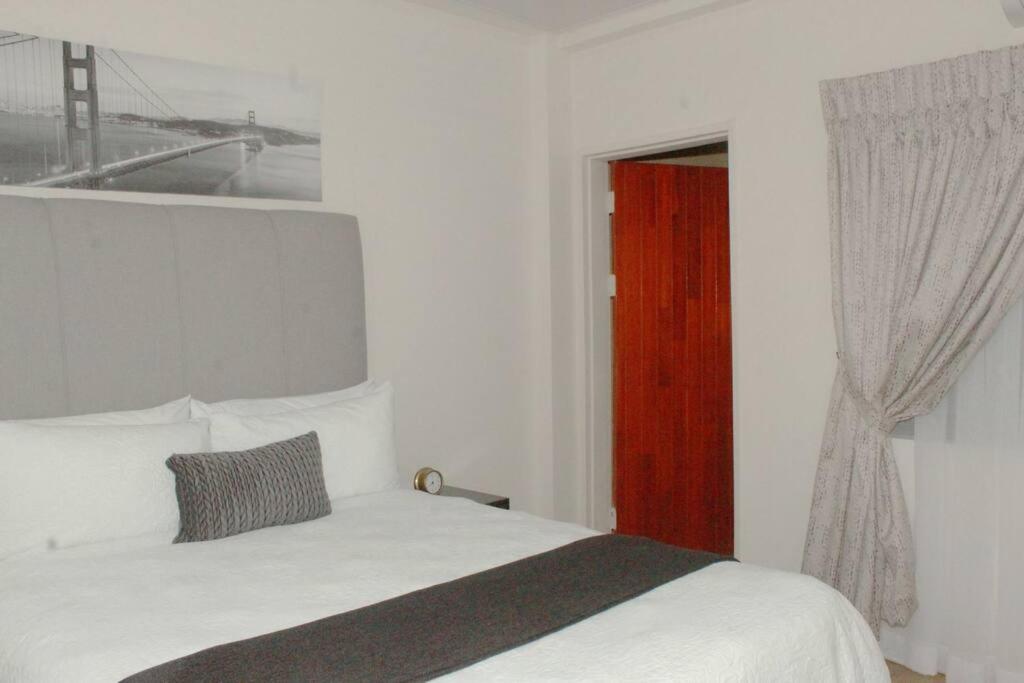 1 dormitorio con cama blanca y puerta roja en Ribbon 210's Two bedroom apartment, en Gaborone
