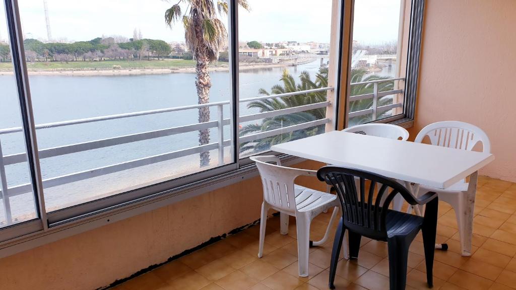 une table et des chaises dans une pièce avec une grande fenêtre dans l'établissement BAIE DES ANGES I Agréable 2 pièces cabine résidence avec piscine vue lagon Richelieu Cap d'Agde, au Cap d'Agde