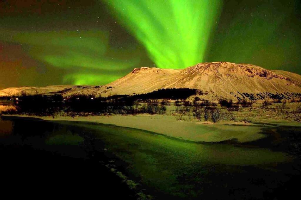 an aurora over a mountain and a body of water at Paradise near Reykjavik w. Sauna - Northern Lights in Mosfellsbær
