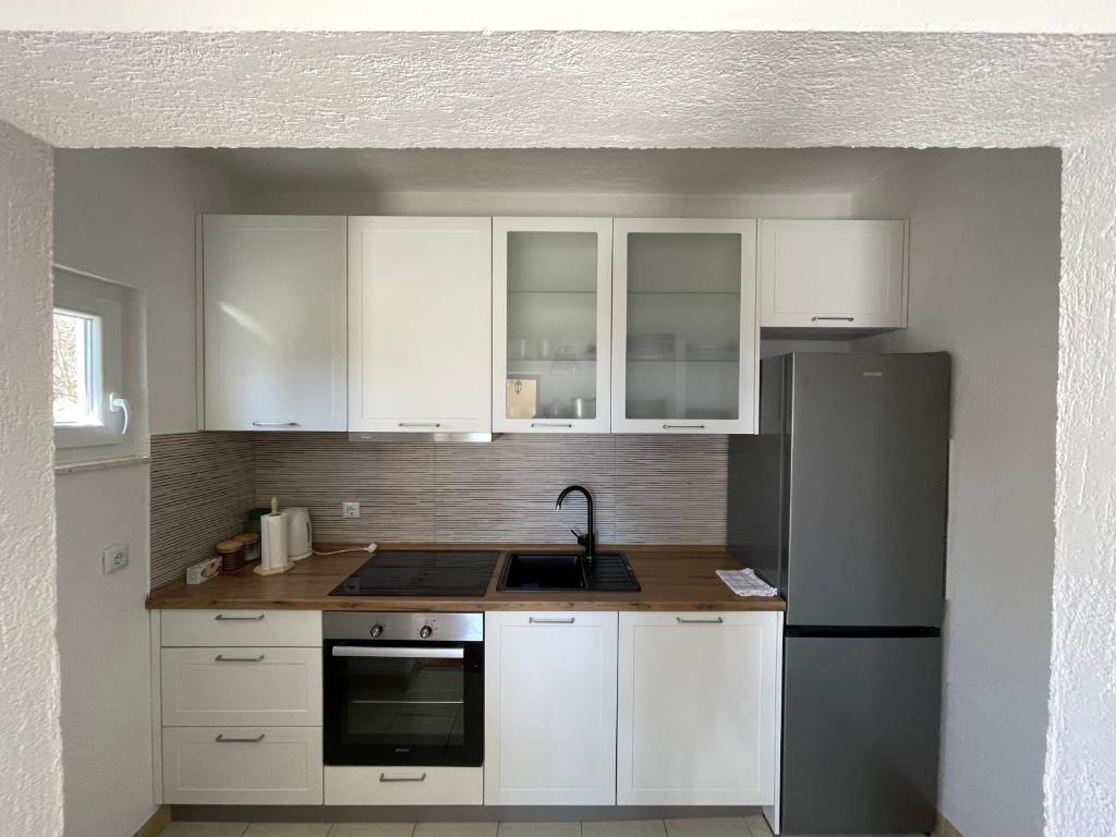 a kitchen with white cabinets and a black refrigerator at Apartman ANA in Vrlika