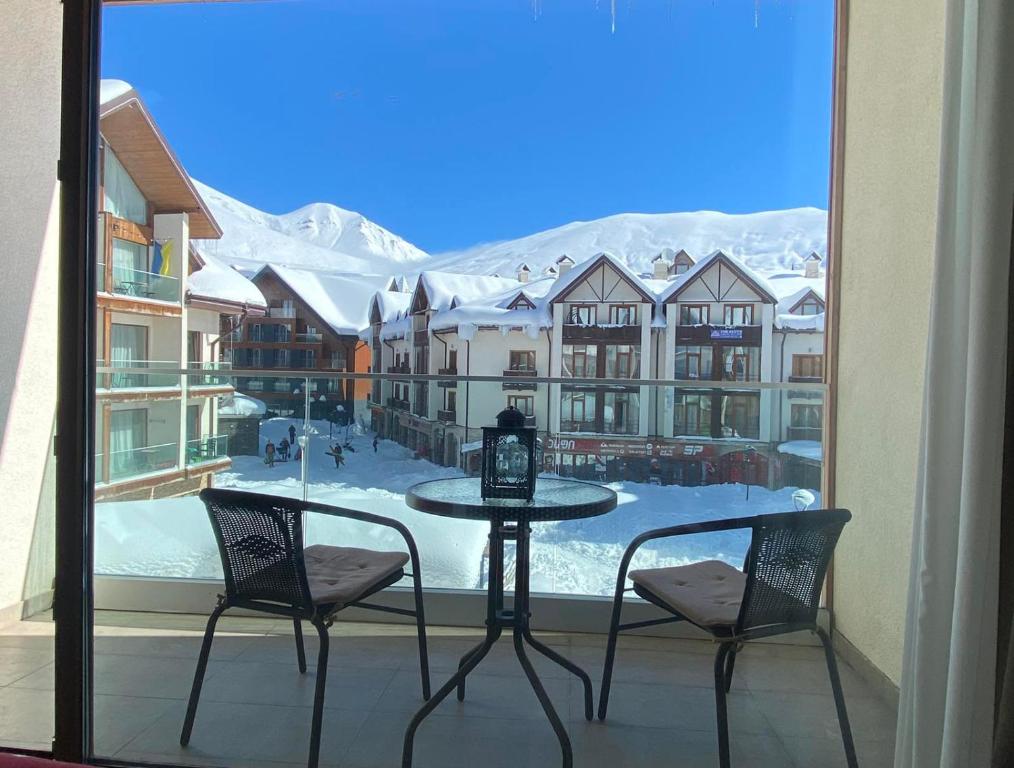 New Gudauri Alpen Apartments في غودواري: طاولة وكراسي على شرفة مطلة على جبل مغطى بالثلج