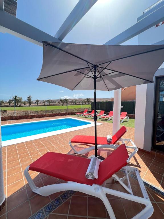 a chair with an umbrella next to a swimming pool at Villa Eva - New to the market, fully refurbished licensed villa - private pool in Caleta De Fuste