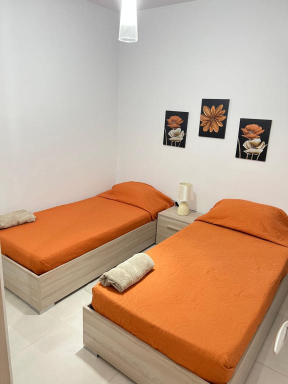 - 2 lits dans une chambre avec des draps en orange et des photos sur le mur dans l'établissement Habitación Doble o sencilla en apartamento Compartido en Gzira Malta , zona centrica, à Il-Gżira