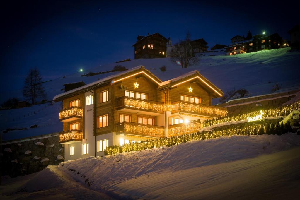 una casa grande con luces en la nieve por la noche en AZapartments Clarino, en Grächen
