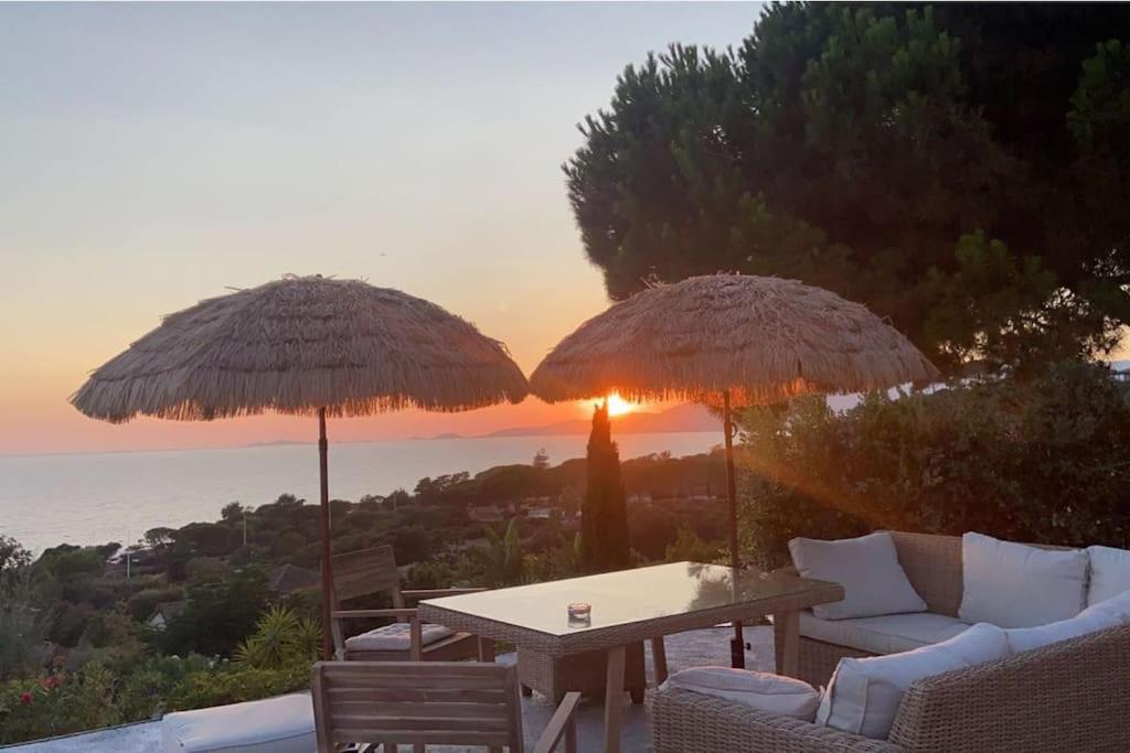 2 Sonnenschirme und ein Tisch und Stühle auf einer Terrasse in der Unterkunft Villa Corse Vue mer et piscine in Porticcio