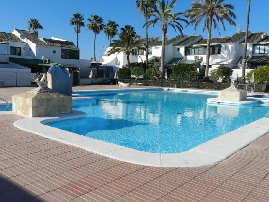 une grande piscine avec des palmiers et des maisons dans l'établissement Entire townhouse in the paradise, à Maspalomas