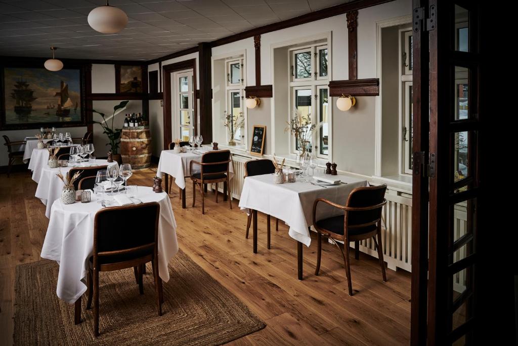 スケーエンにあるHotel Strandly Skagenのテーブルと椅子(白いテーブルクロス付)が備わるレストラン