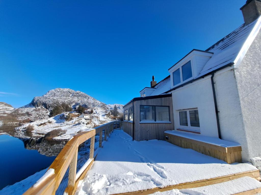 a house in the snow next to a body of water at NC500 - Modern croft house at Handa in Scourie