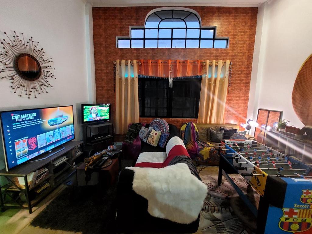 a living room with a person sitting in a chair watching a television at TAAL VIEW: Townhouse with Pool, Netflix, PS4, Foosball, Karaoke in Tagaytay