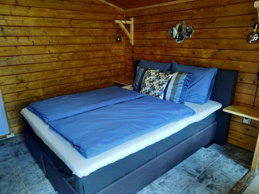 a bed with blue sheets in a room with wooden walls at B&B Paardenhof in Wapenveld