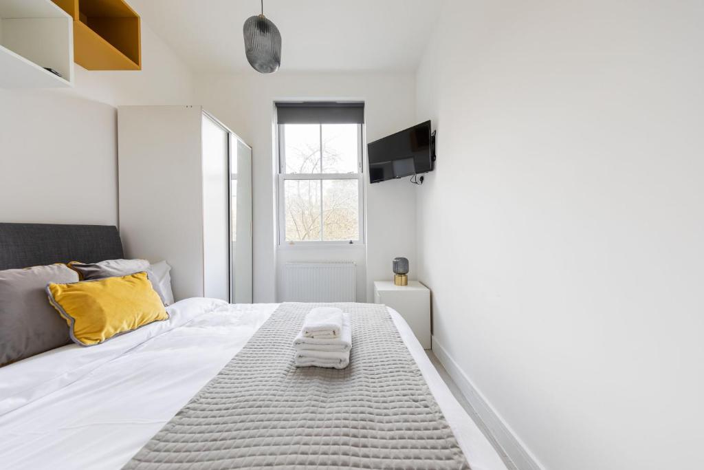 a white bedroom with a bed and a yellow pillow at Cozy Ensuite Bedroom for Two near Tufnell Park in London