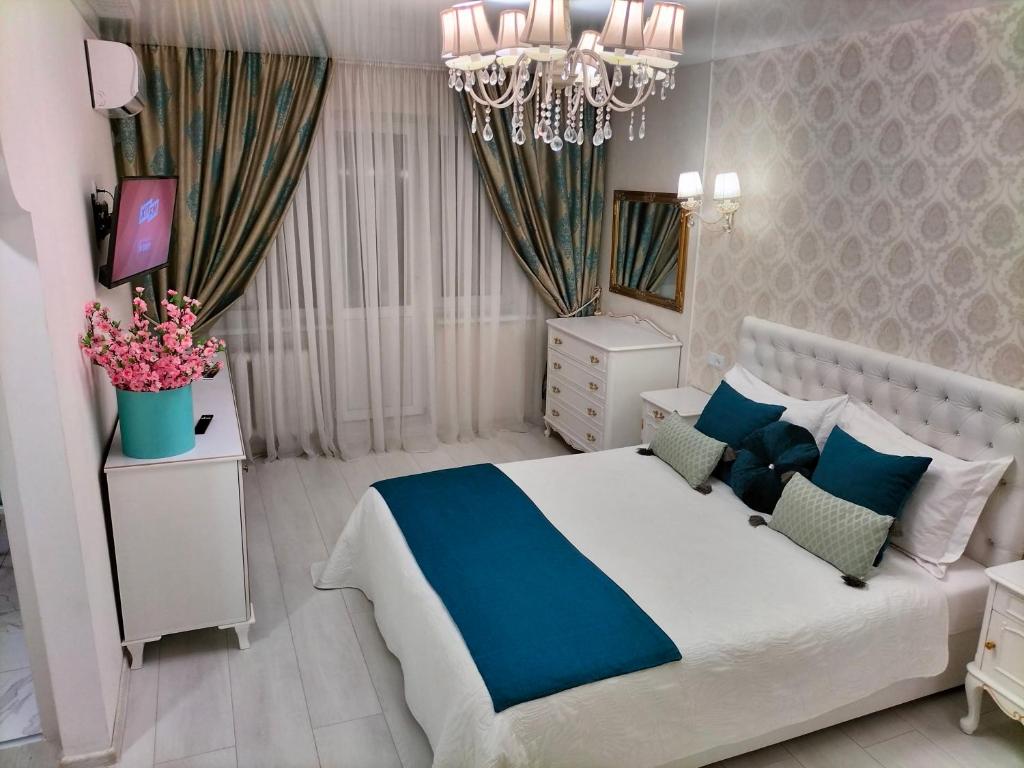 a white and blue bedroom with a bed and a chandelier at VIP Апартаменты in Dnipro