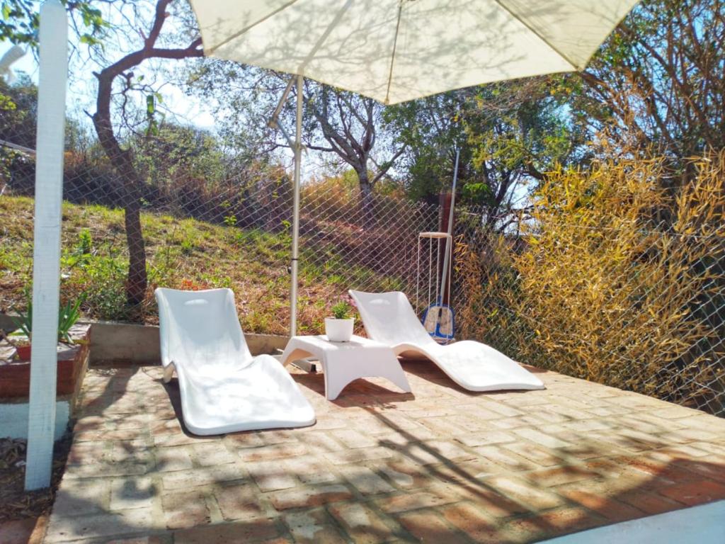 three white chairs and an umbrella on a patio at Encanto Serrano in Salsipuedes
