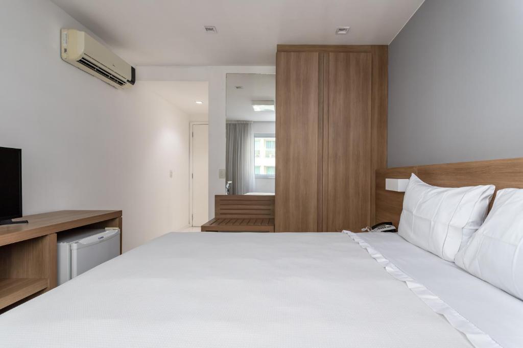 1 dormitorio con 1 cama blanca grande y TV en Flat Barra Da Tijuca, en Río de Janeiro