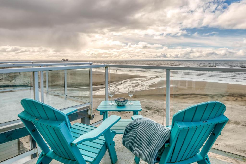 two chairs and a table on a balcony overlooking the beach at Seascape Rockaway - Meredith Lodging in Rockaway Beach