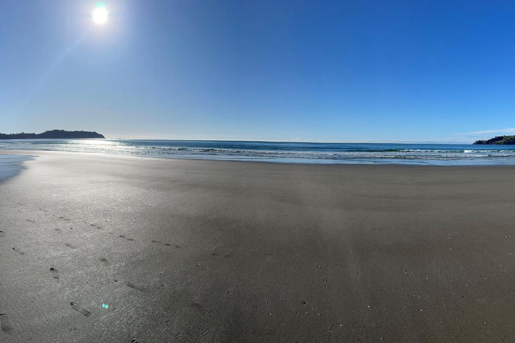 a sandy beach with the ocean in the background at Waiheke Onetangi Close to Beach in Onetangi
