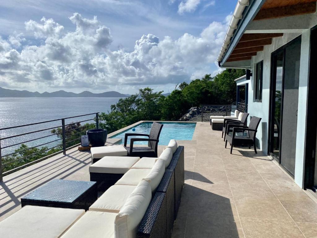 un patio con sillas, una piscina y el océano en Jost Van Dyke, BVI 3 Bedroom Villa with Caribbean Views & Pool en Jost Van Dyke