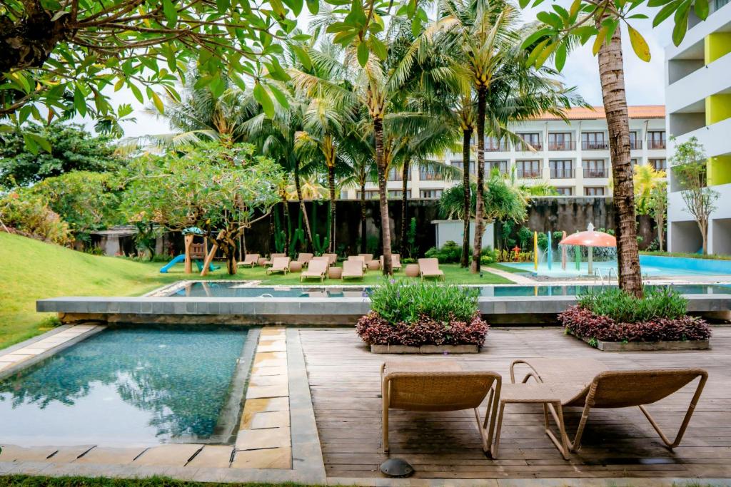 a resort with a swimming pool and palm trees at IKOSHAROLD Resort Benoa in Nusa Dua