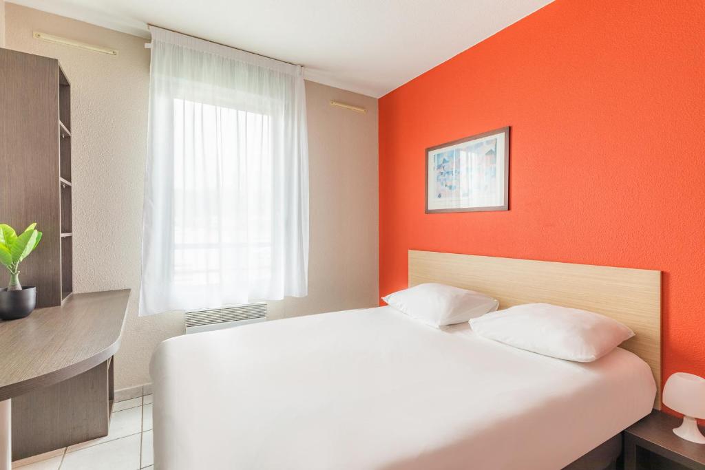 - un lit blanc dans une chambre avec un mur orange dans l'établissement Appart'City Classic Lyon Vaise St Cyr, à Lyon
