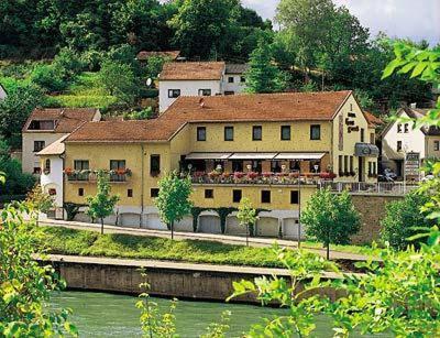 un grand bâtiment jaune à côté d'une rivière dans l'établissement Hotel Haus Schons, à Mettlach