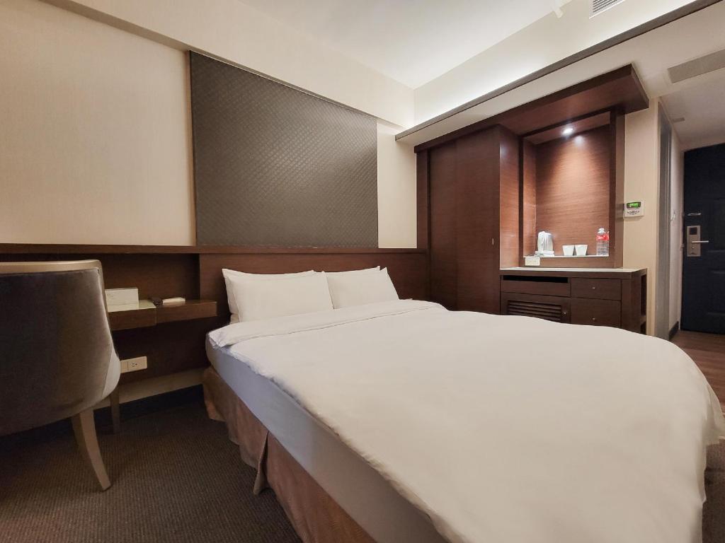 a bedroom with a large white bed and a chair at CHECK inn Express Taichung Fengchia in Taichung