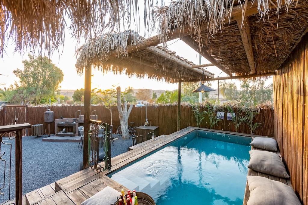 a swimming pool with a thatched roof at הבית החום בערבה in Sappir