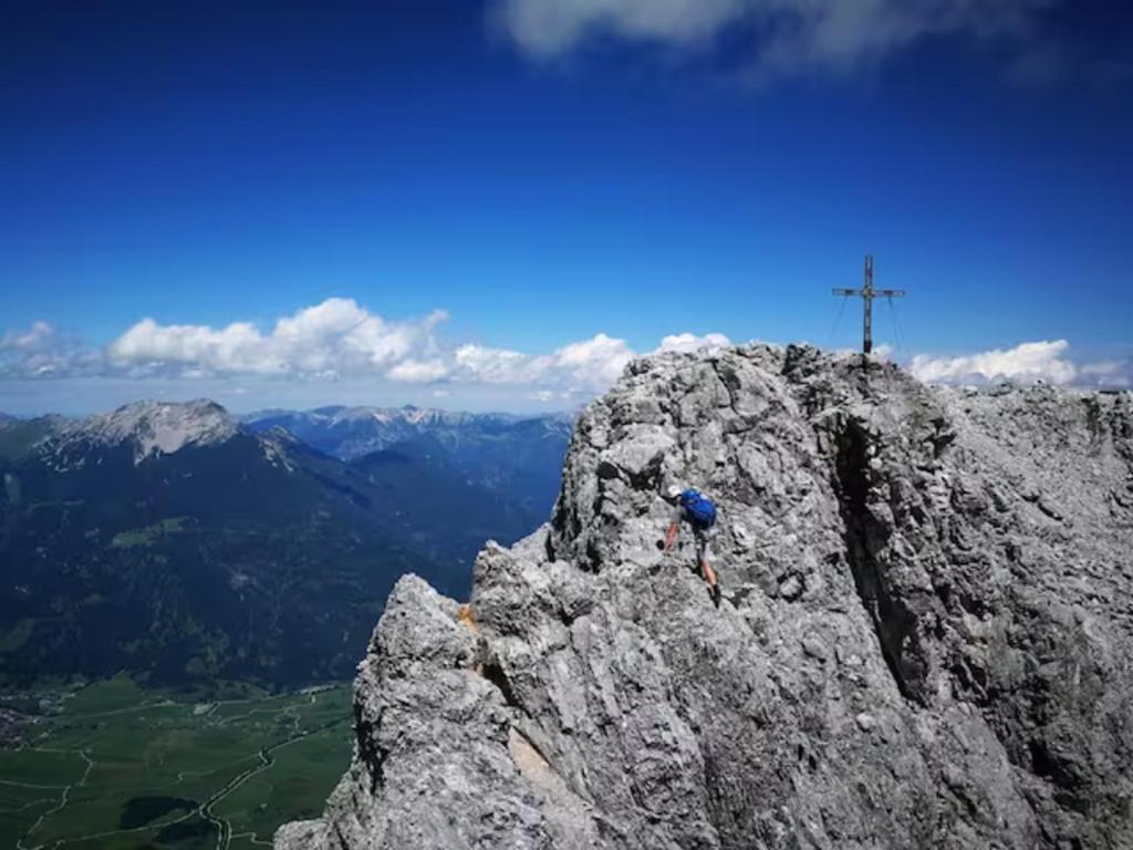 una persona parada en el borde de una montaña rocosa con una cruz en Rad - Wanderparadis Tiroler Zugspitze Arena Ehrwald, en Ehrwald