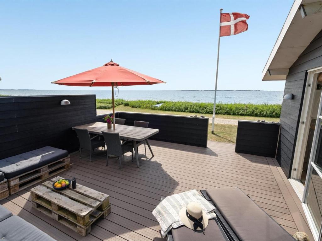 eine Holzterrasse mit einem Tisch und einem Sonnenschirm in der Unterkunft Holiday Home Akseline - 20m from the sea in Funen by Interhome in Assens