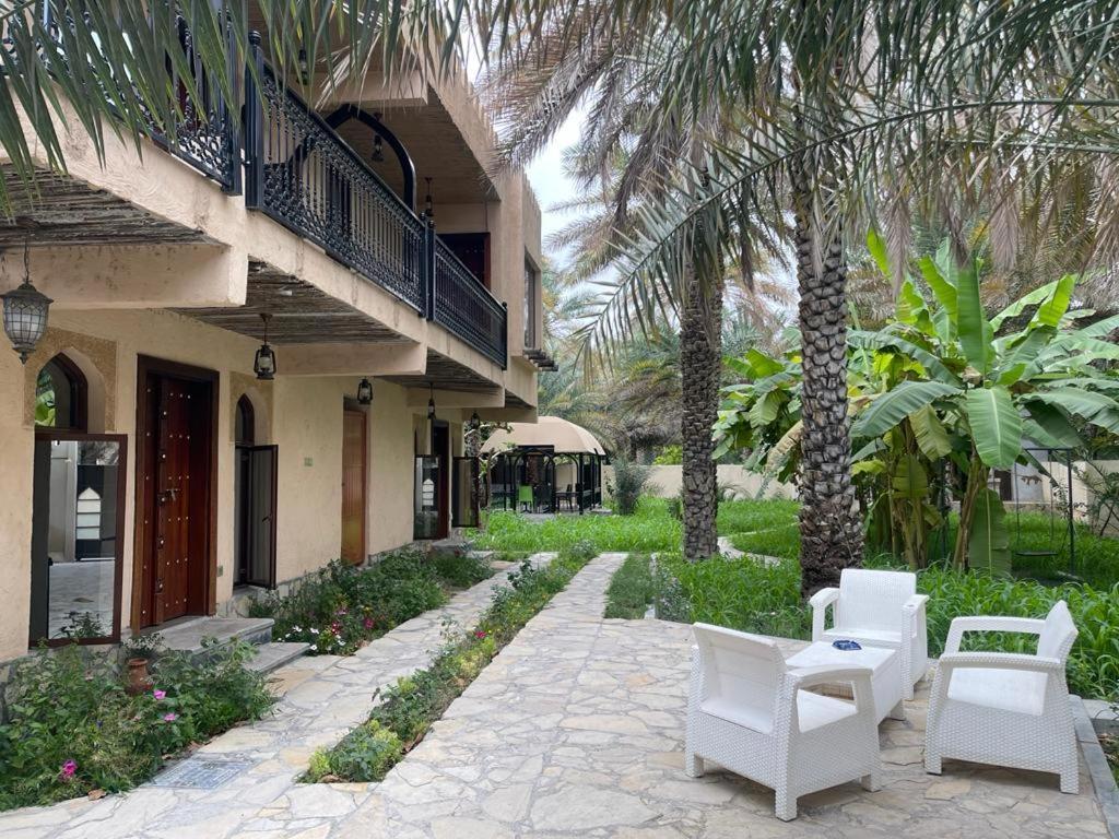 eine Terrasse mit weißen Stühlen und Palmen neben einem Gebäude in der Unterkunft Date Palm Inn in Nizwa