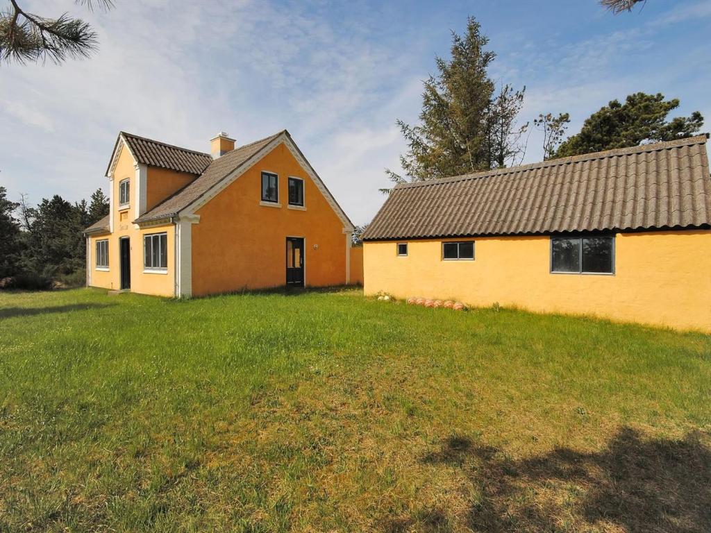 una casa amarilla en un campo de hierba junto a una casa en Holiday Home Margrethe - 1-1km from the sea in NW Jutland by Interhome, en Bedsted Thy
