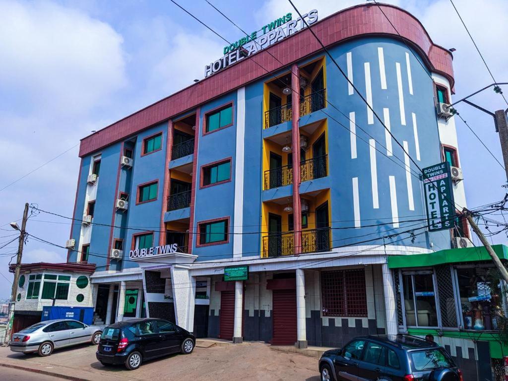 un bâtiment avec des voitures garées devant lui dans l'établissement Double twins Hotel & appartement, à Yaoundé