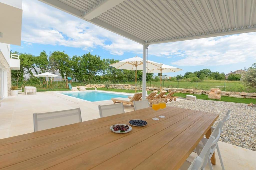 Villa Lu by IstriaLux في Prkačini: طاولة خشبية مع كراسي ومظلة ومسبح
