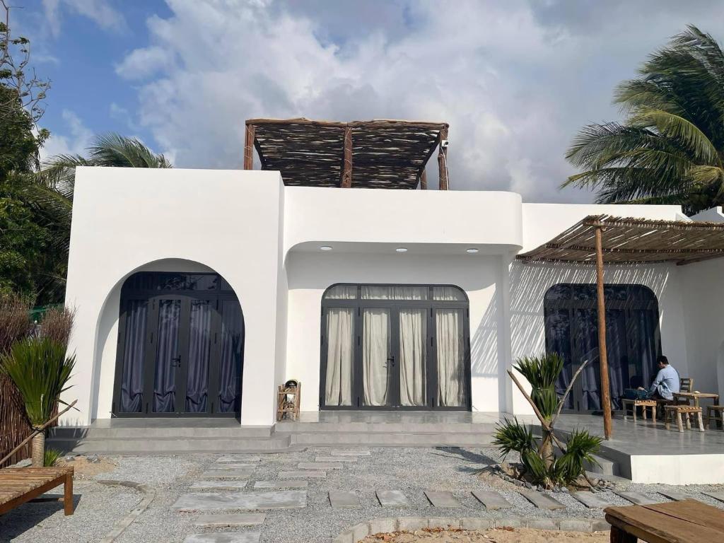 une maison blanche avec des portes noires et un homme assis à une table dans l'établissement My Hoa Oceanfront Home, à Ấp Mỹ Hải