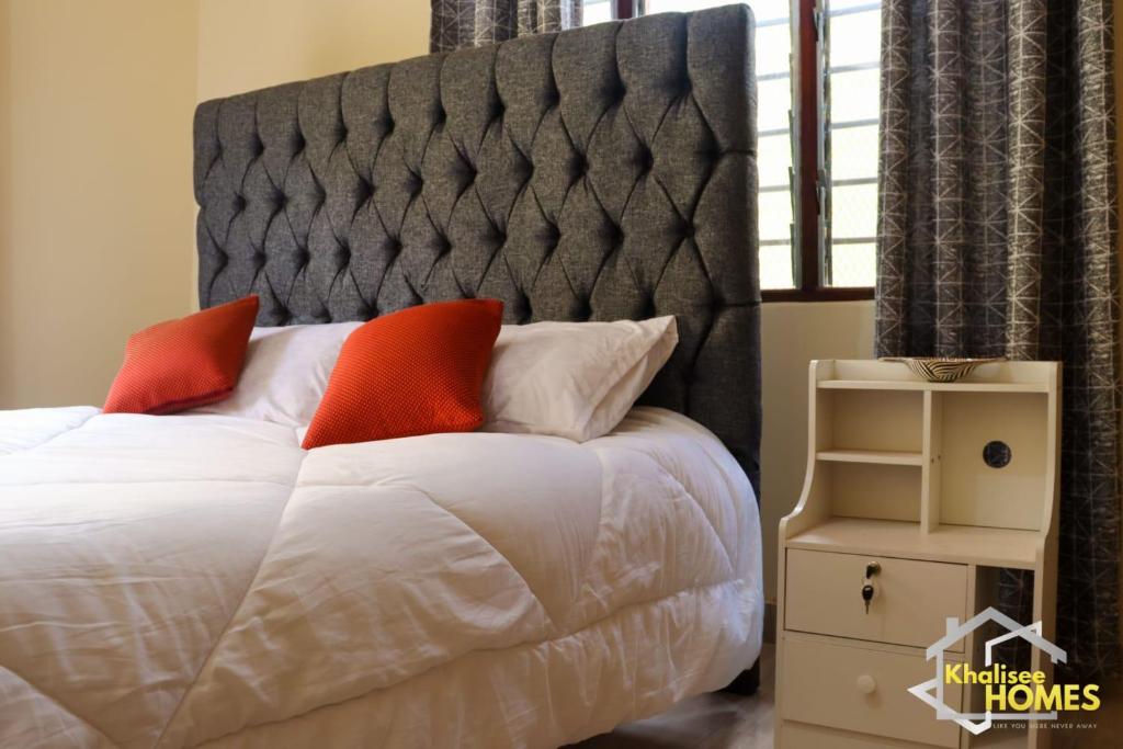 a bed with a gray headboard and orange pillows at Khalisee Homes Studio apartment in Voi
