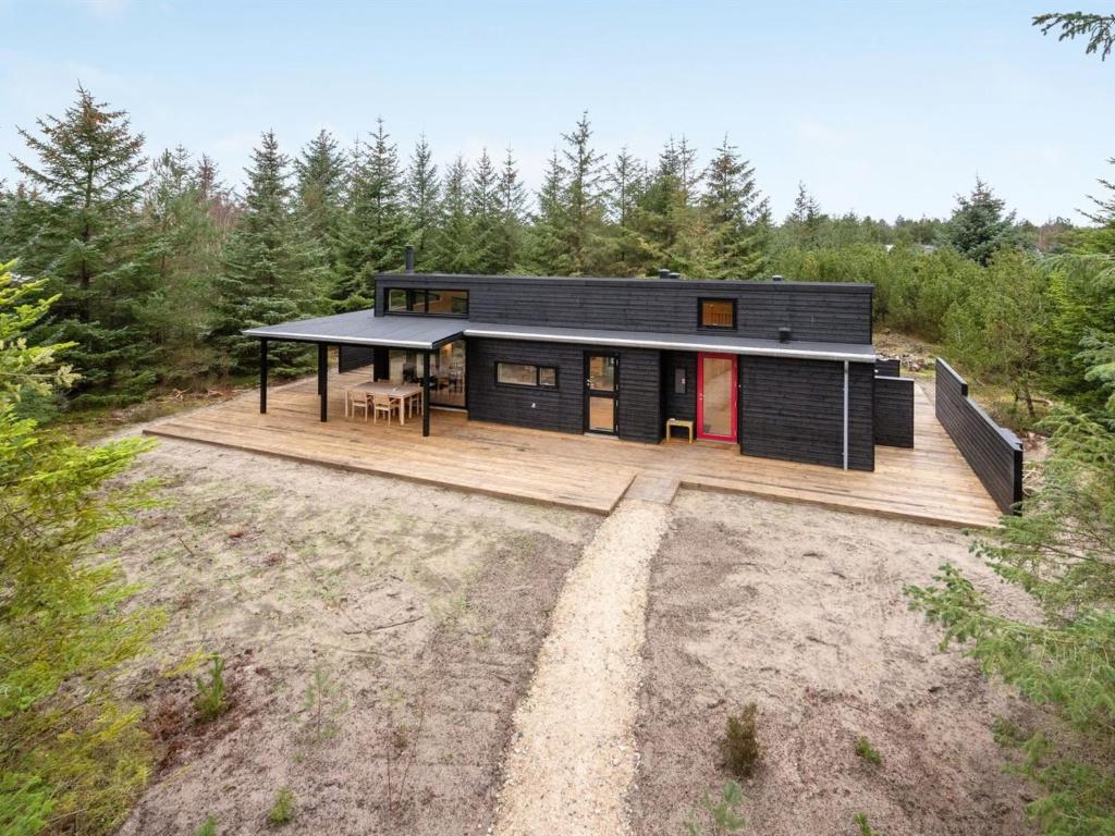 una casa negra con terraza de madera en el bosque en Holiday Home Gunnor - 1-3km from the sea in NW Jutland by Interhome en Fjerritslev