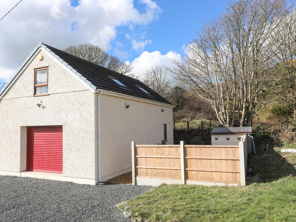 a white garage with a red door and a fence at Cwt Ci in Llangefni