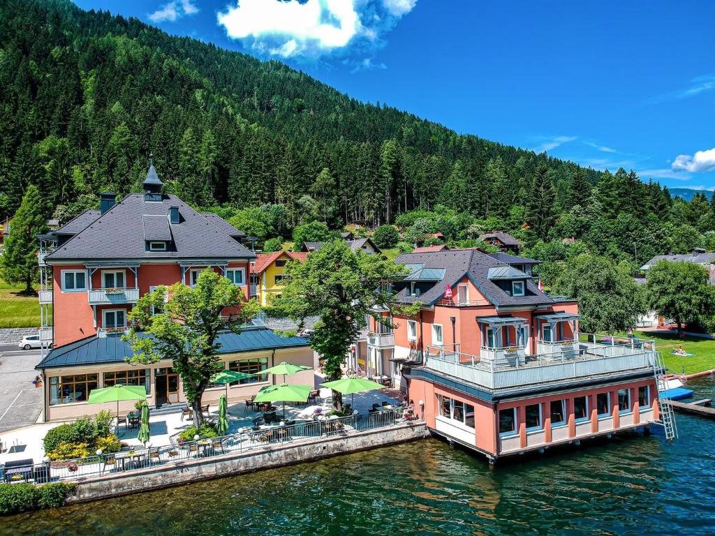 ein großes Haus auf dem Wasser mit einem Boot in der Unterkunft Strandhotel Burgstaller in Feld am See