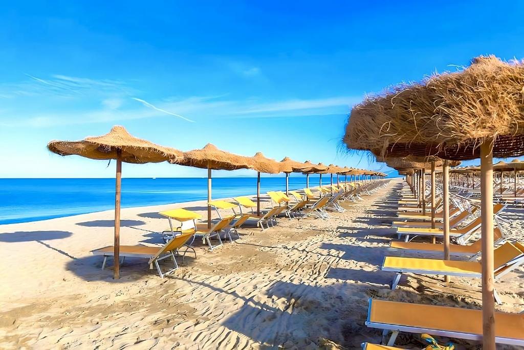 una fila de sillas y sombrillas en una playa en Regina Del Mare Holiday Apartments en Tirrenia