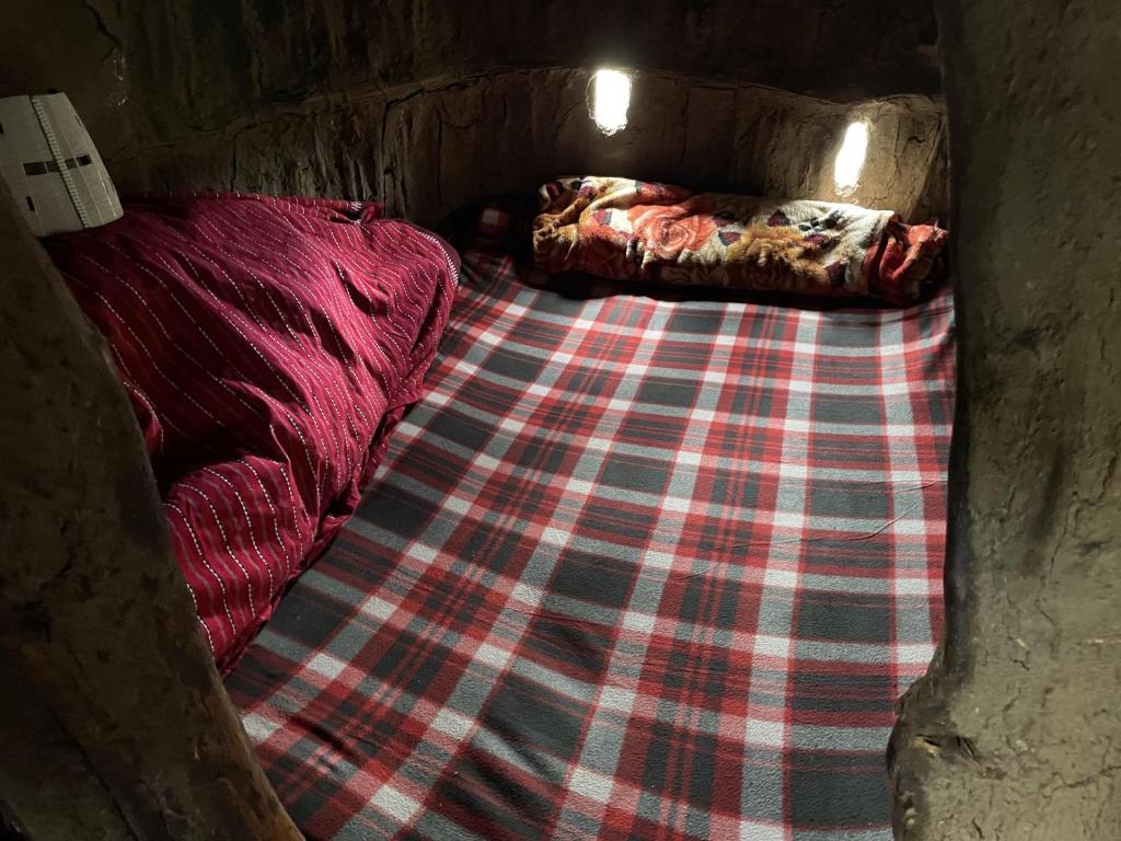 a small bed in a room with a plaid blanket at DUPOTO HOMESTAY VILLAGE - MASAI VILLAGE (BOMA) in Mto wa Mbu
