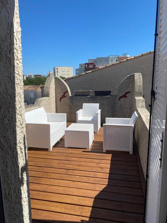 - un balcon avec des chaises blanches sur une terrasse en bois dans l'établissement SAMARIA VILLAGE Magnifique appartement 8 personnes Rochelongue Cap d'Agde, au Cap d'Agde