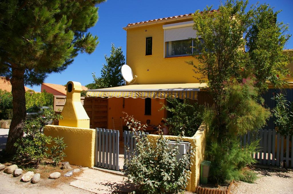 a yellow house with a fence and trees at LeWindy Barcares Terrasse Confort Calme Fibre Vélos Bord Lac Proximité Plage Lydia Coudalere in Le Barcarès